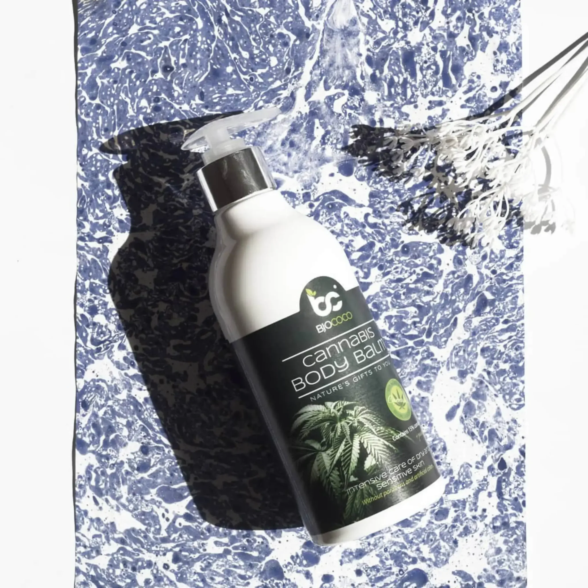 Balsam do ciała BjoCoco na bazie oleju konopnego, umieszczony na tle w stylu marmurowym z delikatnymi białymi kwiatami w tle.