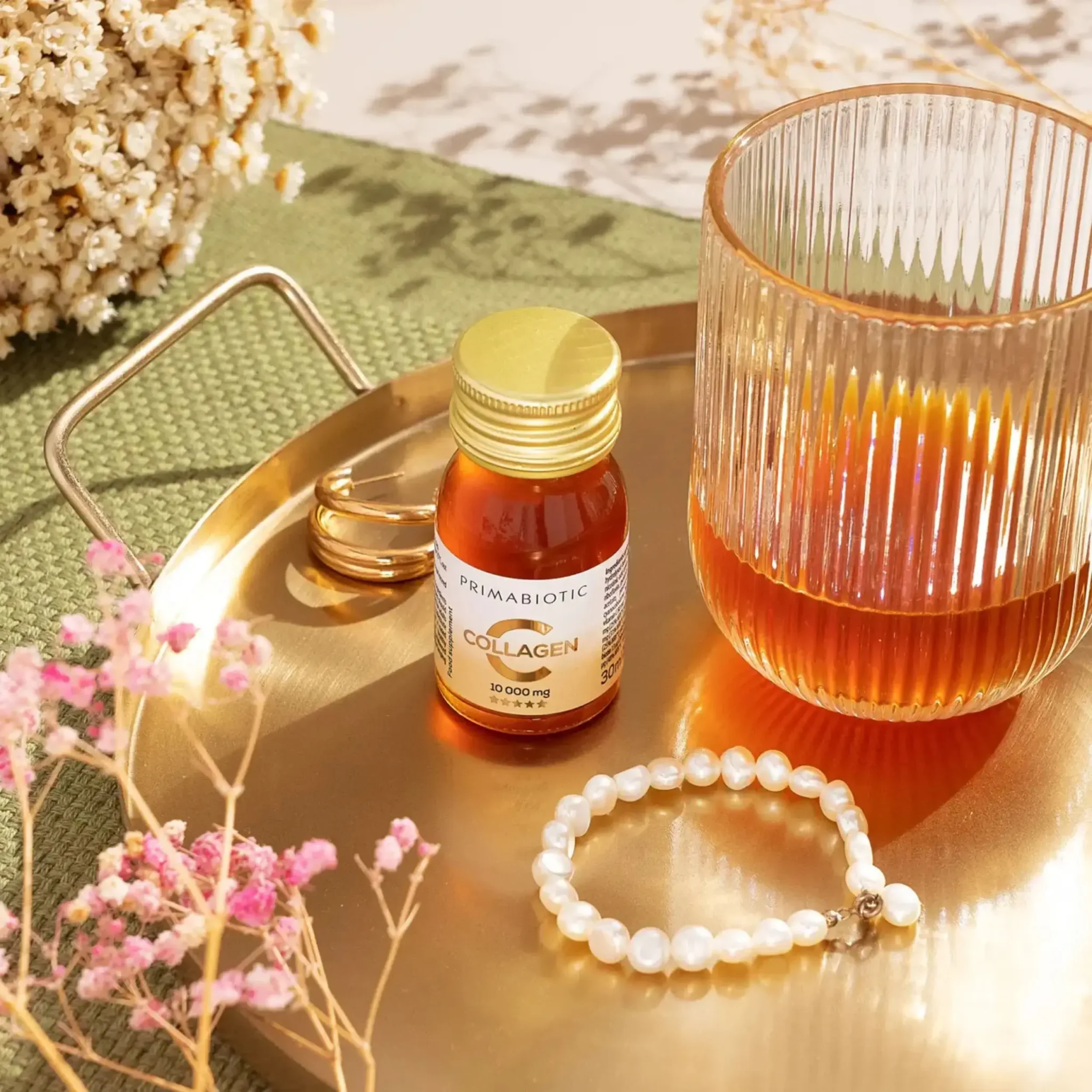 Zestaw kolagenu Primabiotic w buteleczkach i opakowaniu, ustawiony na stole z dekoracjami.