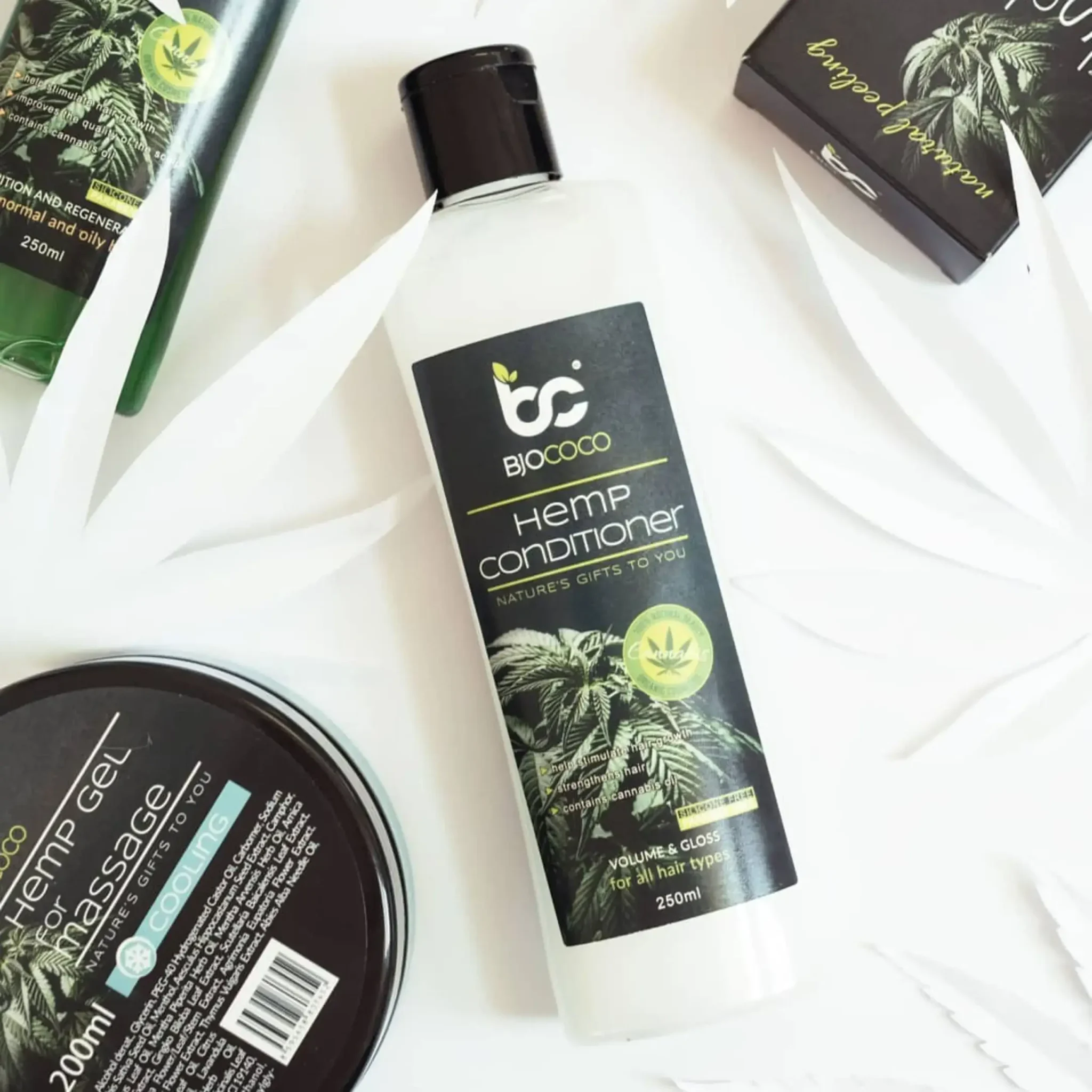 Butelka odżywki konopnej BjoCoco w otoczeniu innych produktów marki, ułożonych na jasnym tle z liśćmi jako dekoracją.