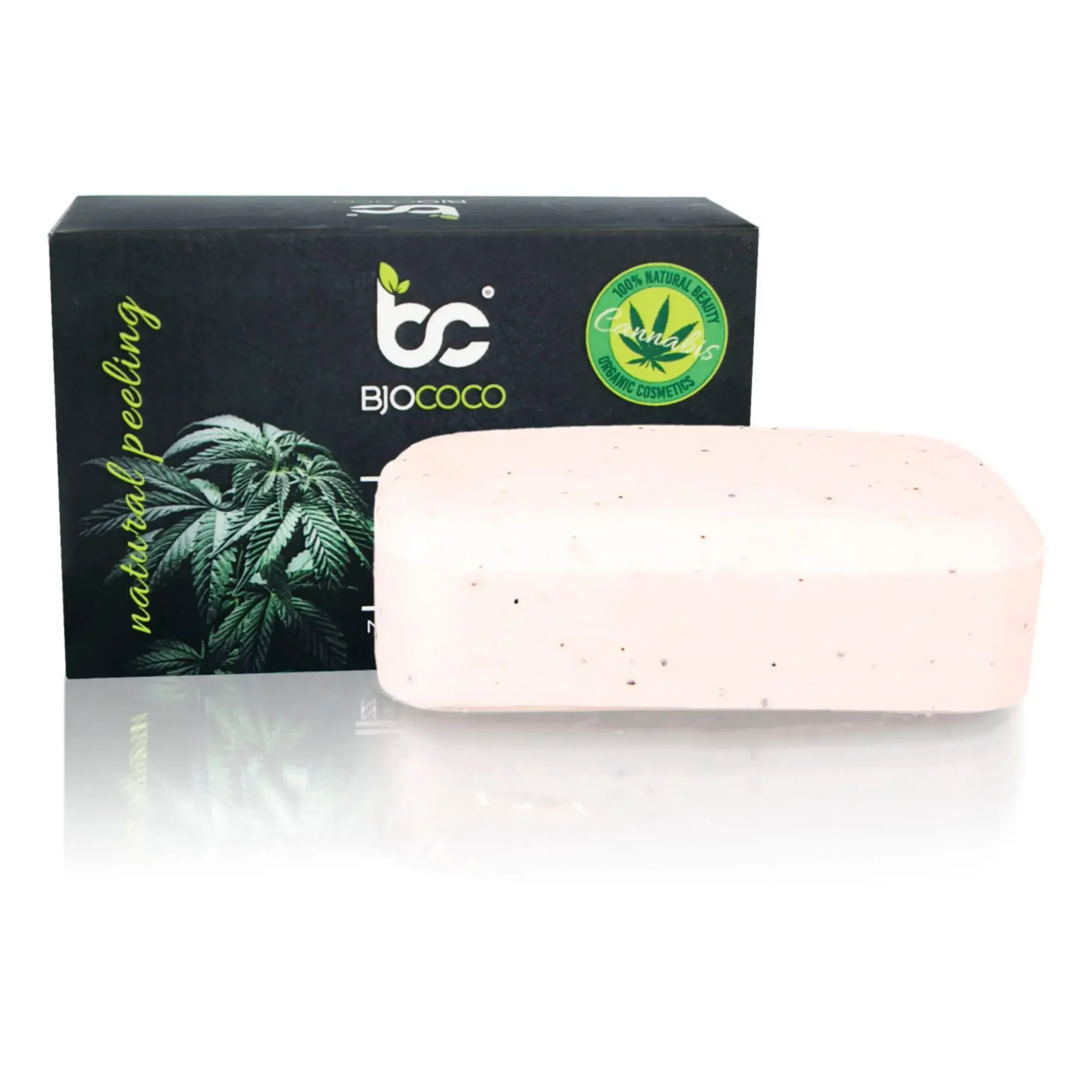 Kostka mydła konopnego BjoCoco z naturalnym peelingiem, ustawiona przed kartonowym opakowaniem, na białym tle.