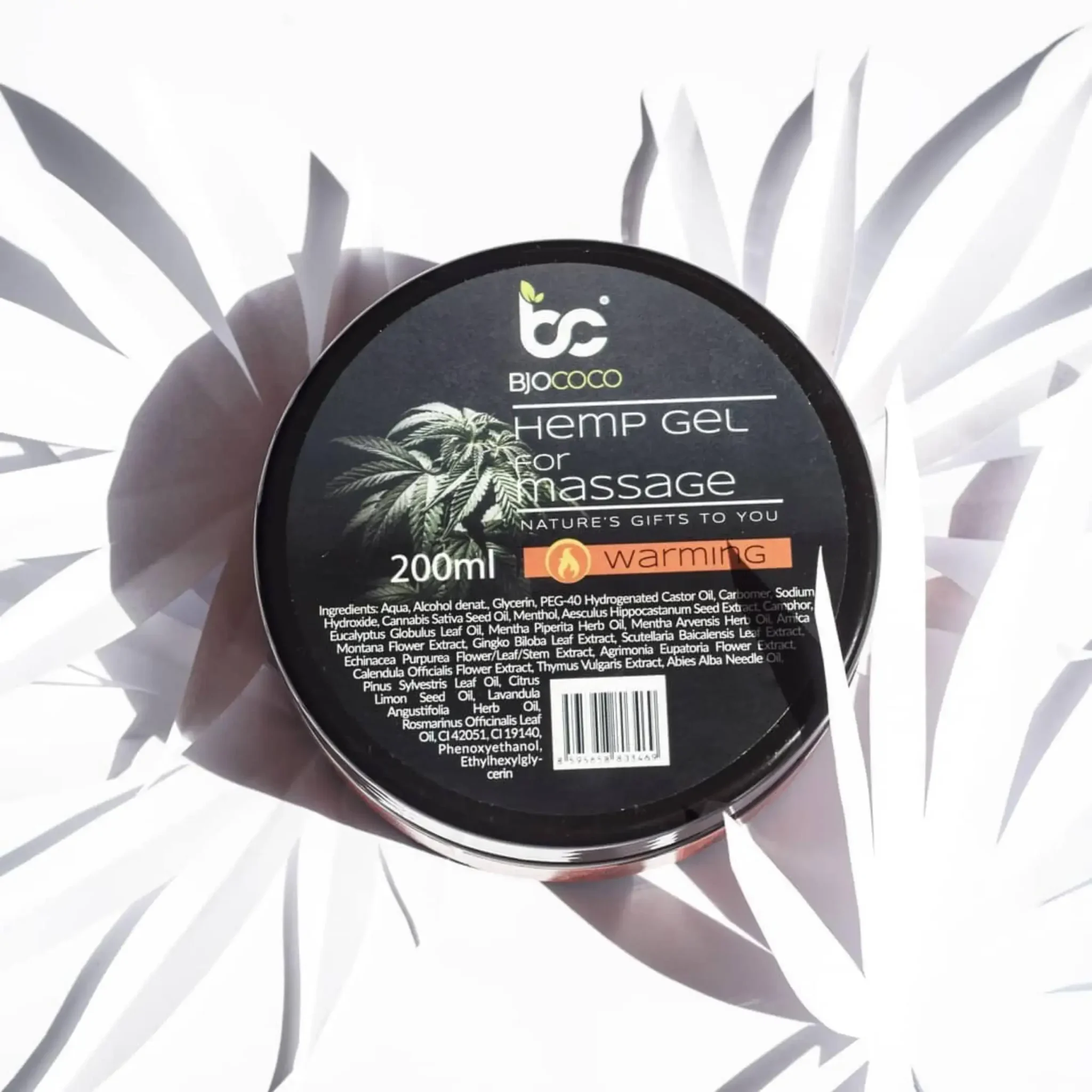 Produkt BjoCoco - rozgrzewający żel konopny w czarnym opakowaniu o pojemności 200 ml, sfotografowany na jasnym tle z dekoracyjnymi liśćmi konopi.