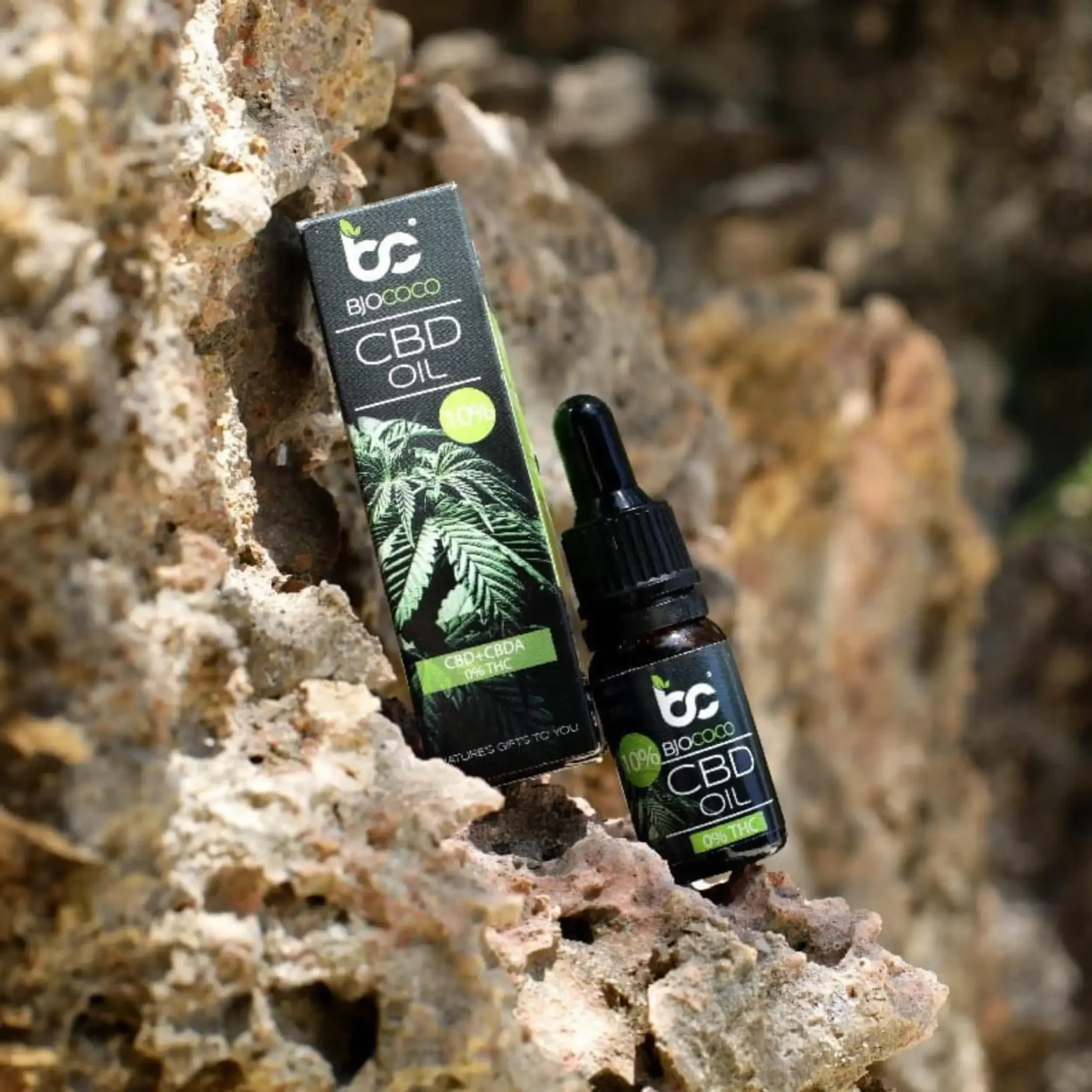 Olejek CBD BjoCoco w ciemnej butelce i jego opakowanie, ustawione na tle naturalnych skał, ukazujące ekologiczny charakter produktu.